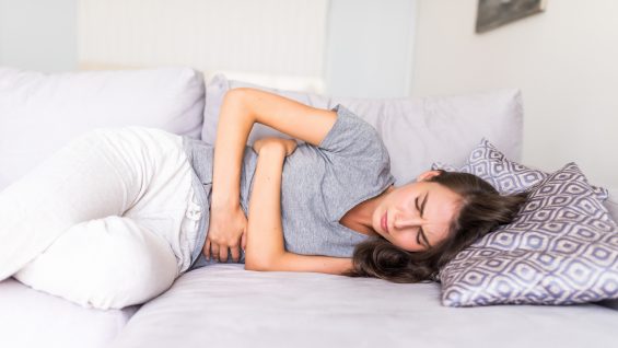 Young woman have abdominal pain because of menstruation lying in couch and holding her stomach.