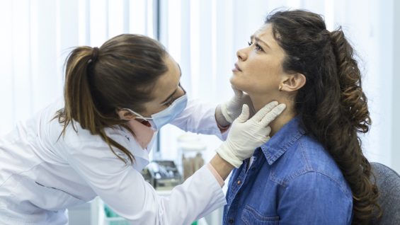 Endocrinologist examining throat of young woman in clinic. Women with thyroid gland test . Endocrinology, hormones and treatment. Inflammation of the sore throat